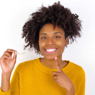 Woman pointing to her smile while holding her Invisalign tray